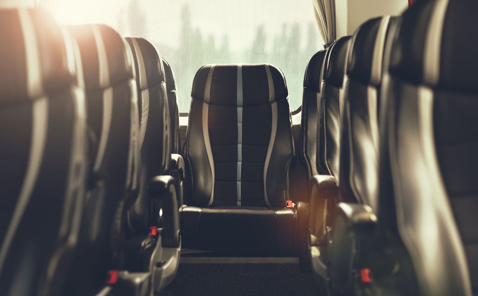 Empty black bus seats in a row with a bright window at the end.