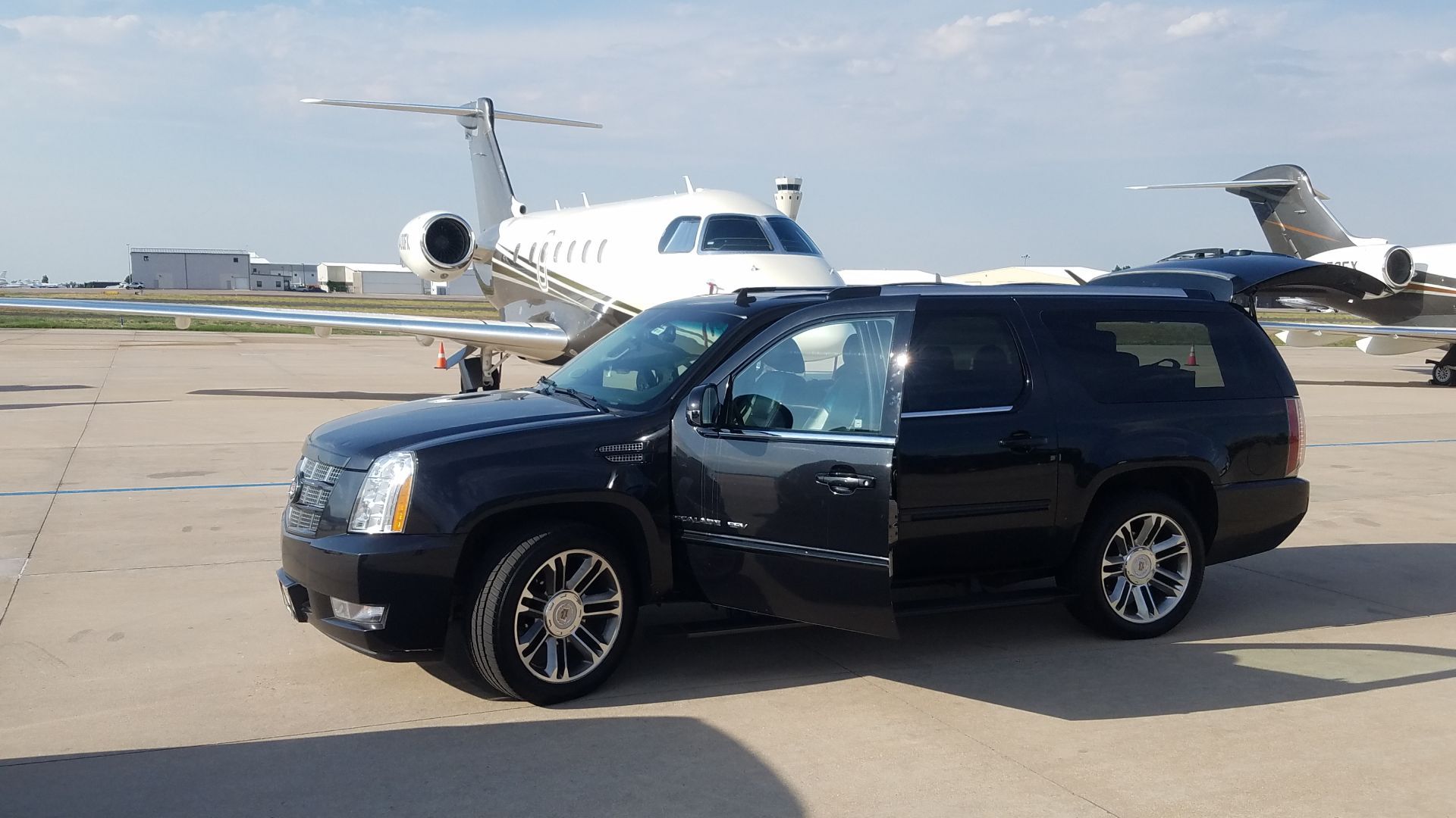Black SUV with open door on airport tarmac, private jet in the background.