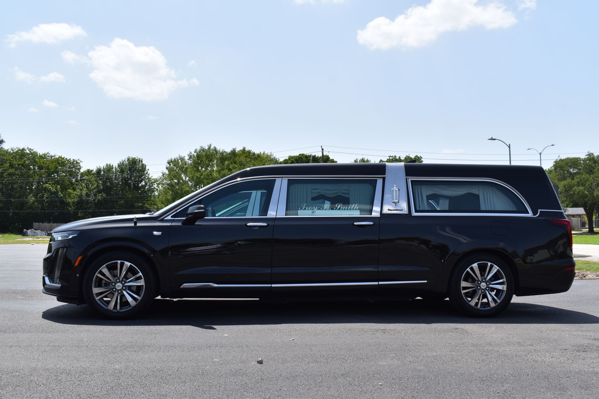 Black hearse on asphalt road, under a partly cloudy sky.