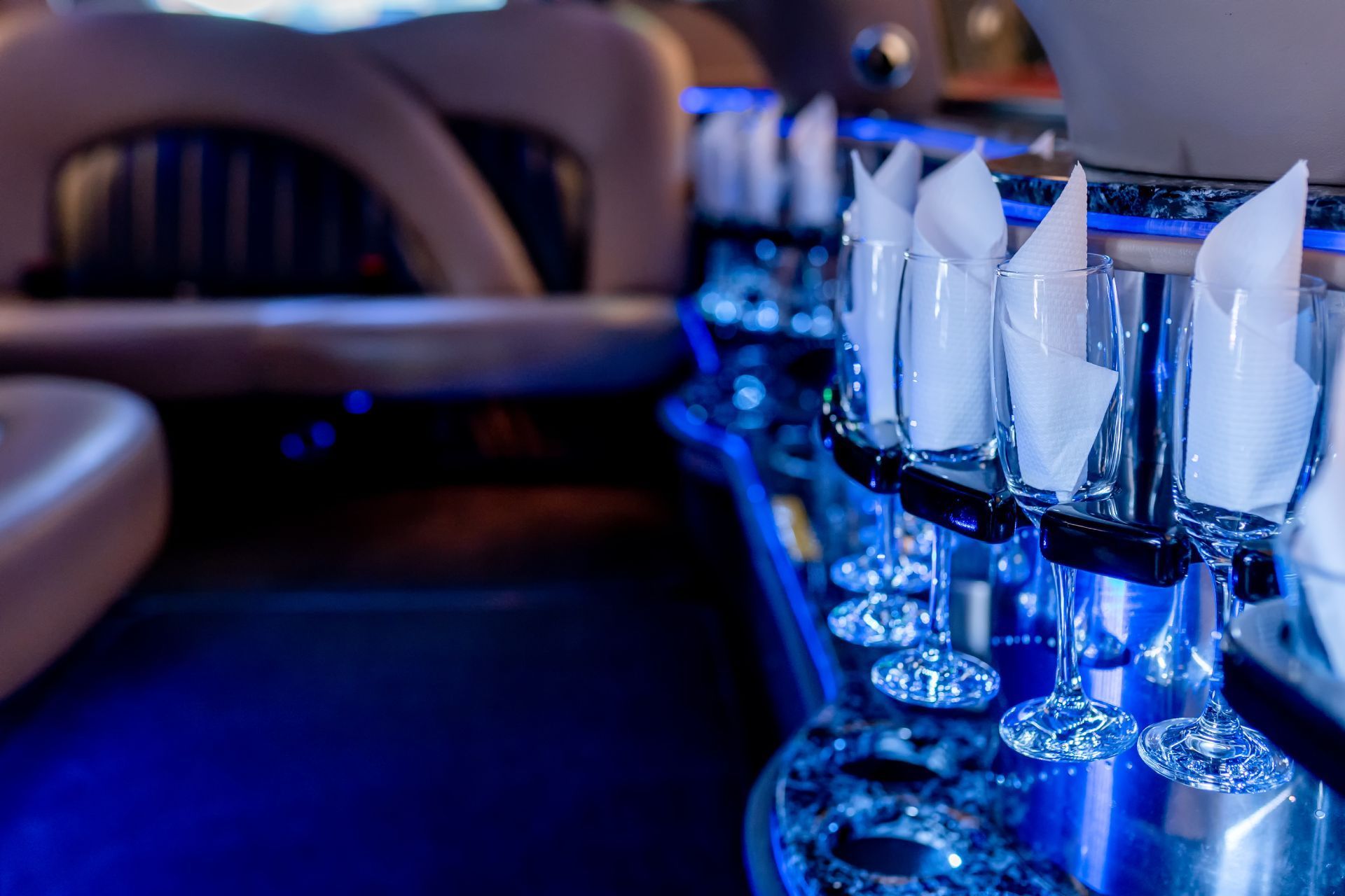 Inside a limousine, champagne flutes with napkins lined up, illuminated with blue lights.
