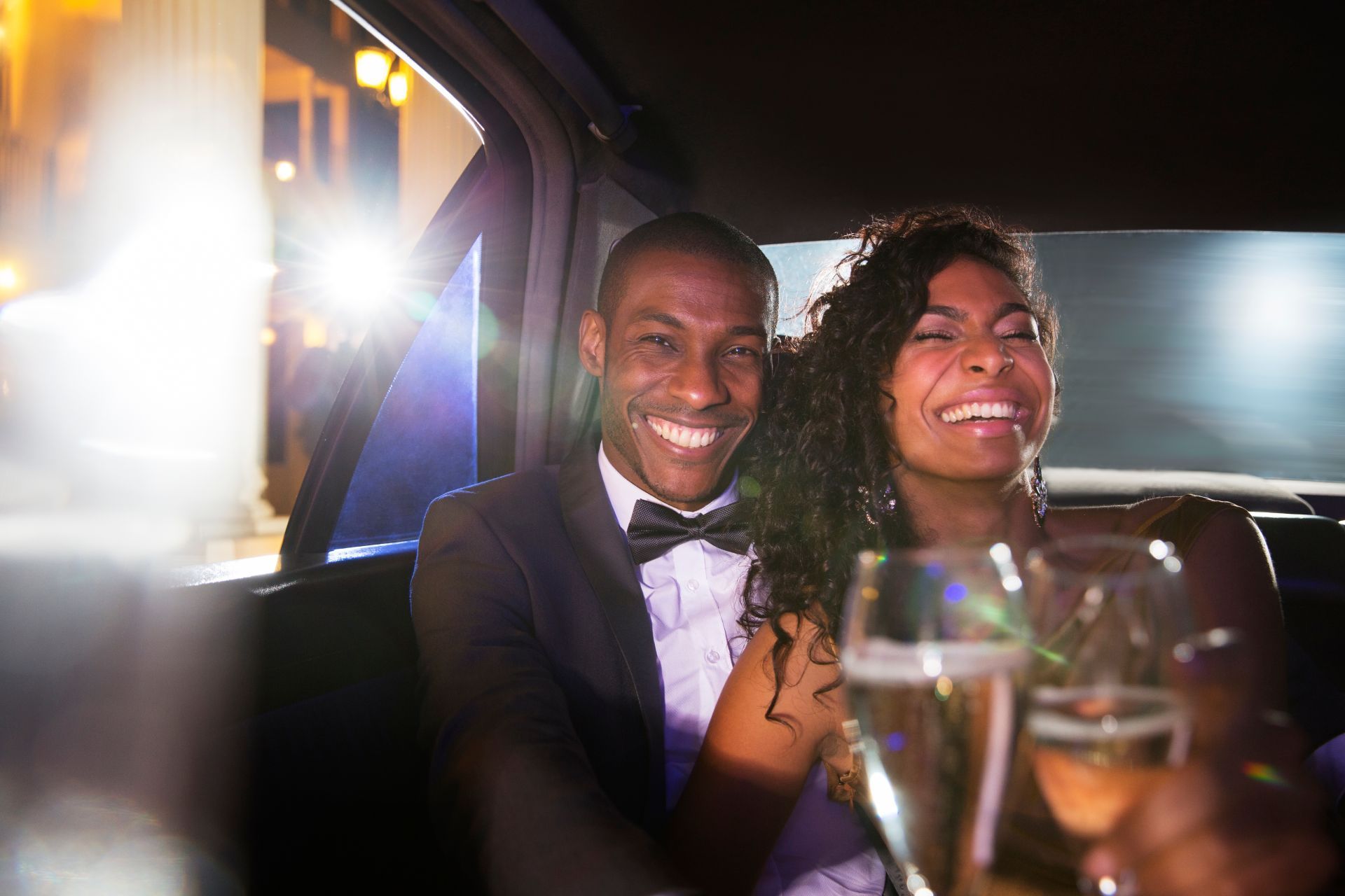 Couple in formal attire smiling and toasting champagne in a limousine.