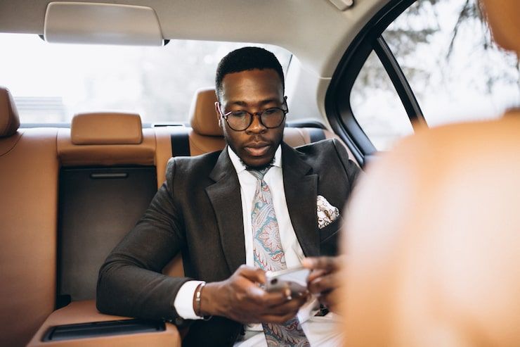 Man in suit using phone in a car, with tan leather interior.