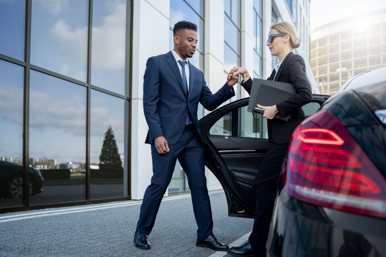Man in suit helps woman exit a black car near a building.