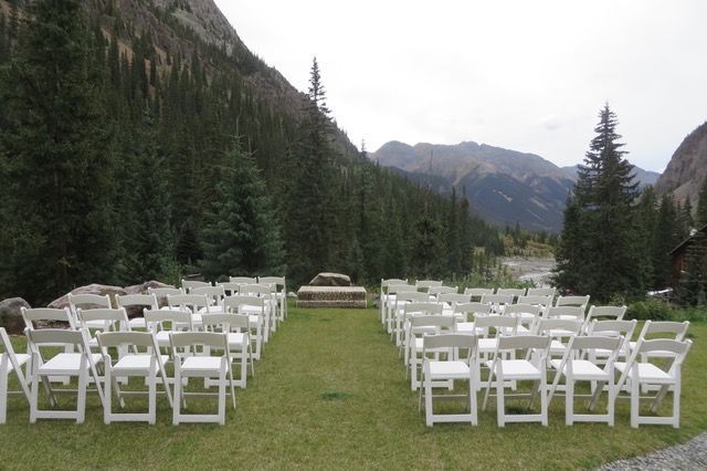 a row of white folding chairs in a field with mountains in the background