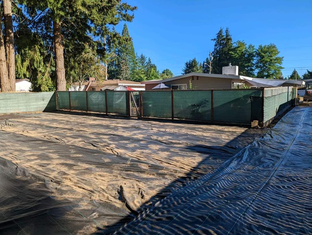 A fence is surrounding a dirt field in front of a house.