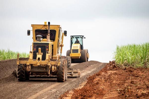 A bulldozer and a tractor are driving down a dirt road.