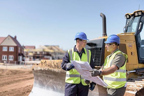 Two construction workers are looking at a blueprint on a construction site.