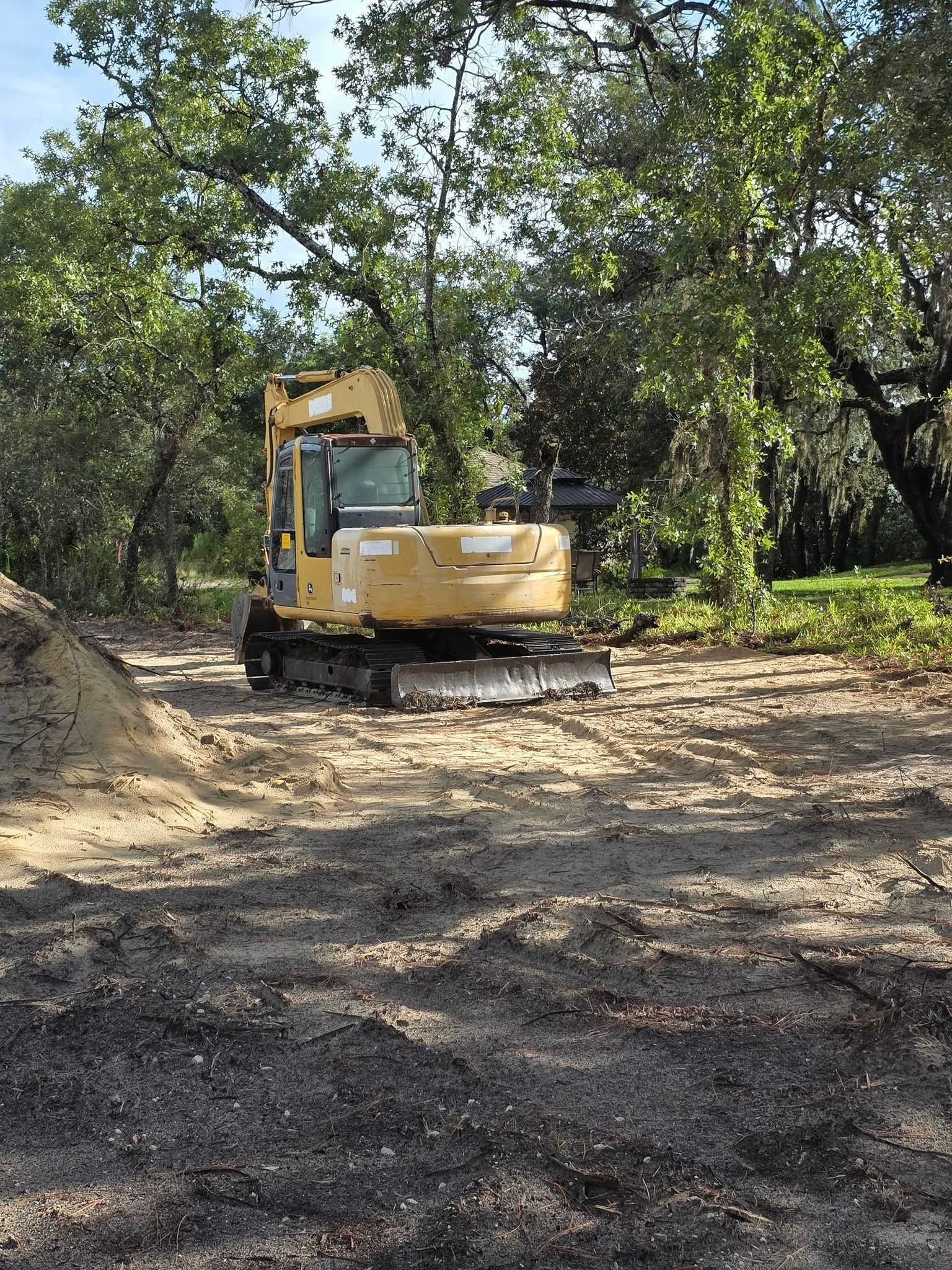 Yellow excavator parked on dirt path in wooded area.