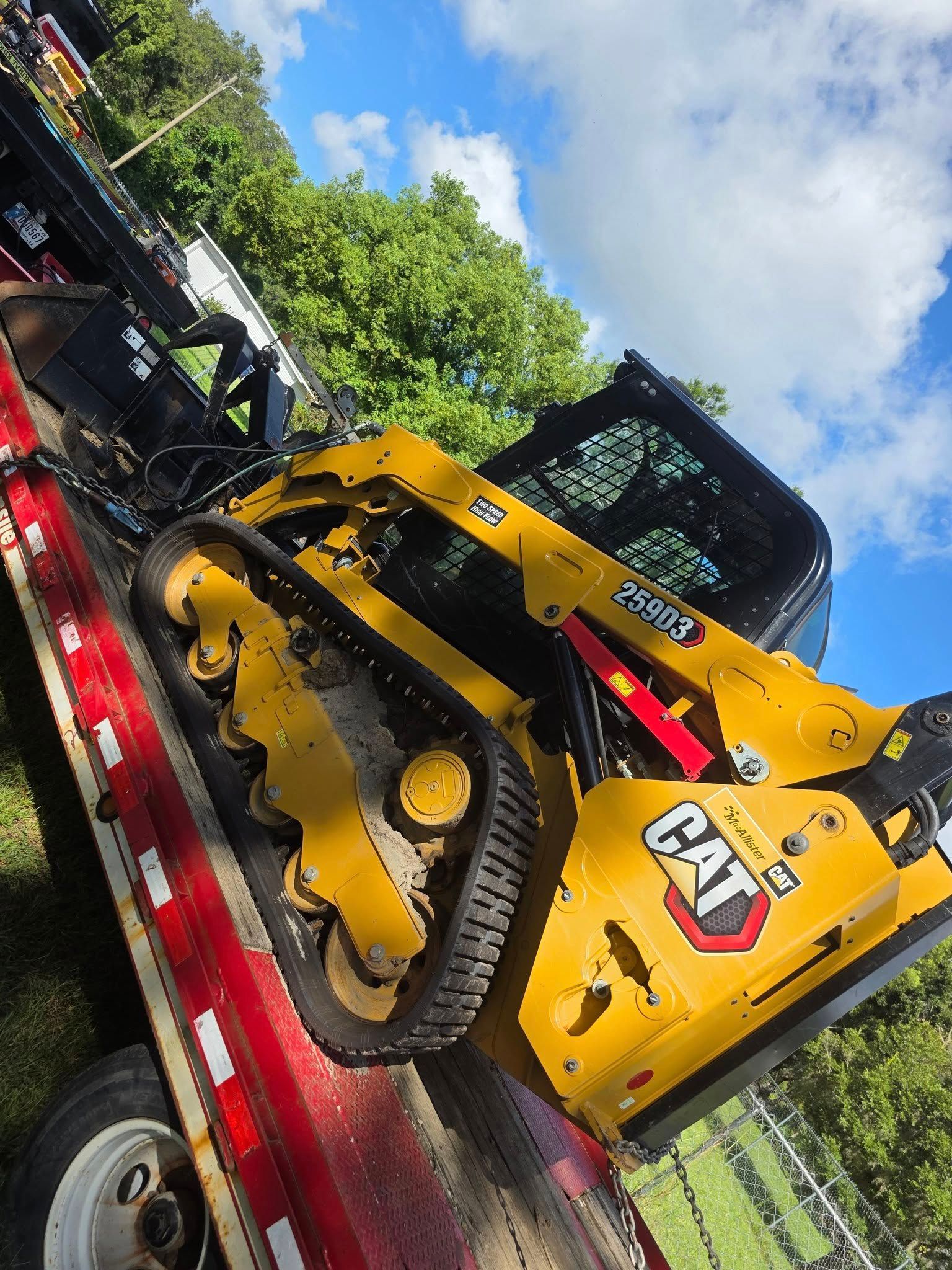 Yellow Caterpillar compact track loader on a trailer against a blue sky.