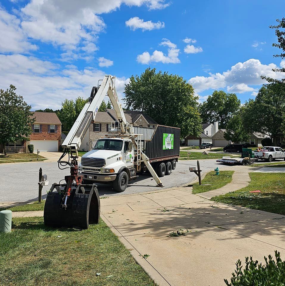 Tree service truck parked on a residential street; crane arm extended, debris.