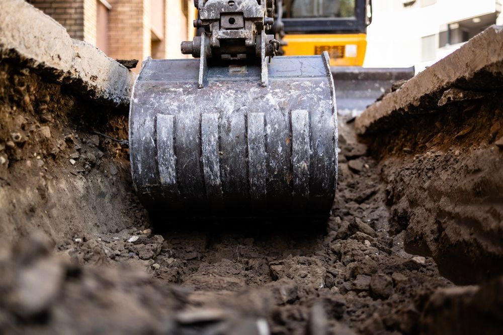 Excavator bucket digging a trench in the dirt.