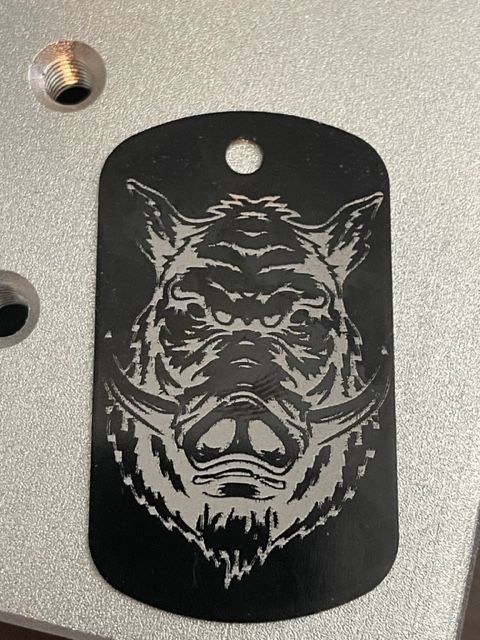 A black dog tag with a picture of a boar on it