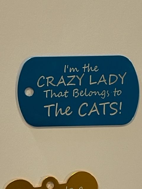 A blue tag that says i 'm the crazy lady that belongs to the cats