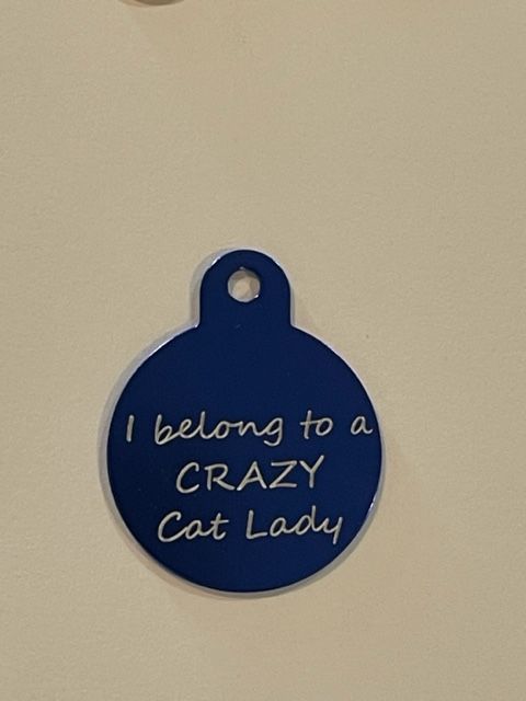 A blue tag that says i belong to a crazy cat lady