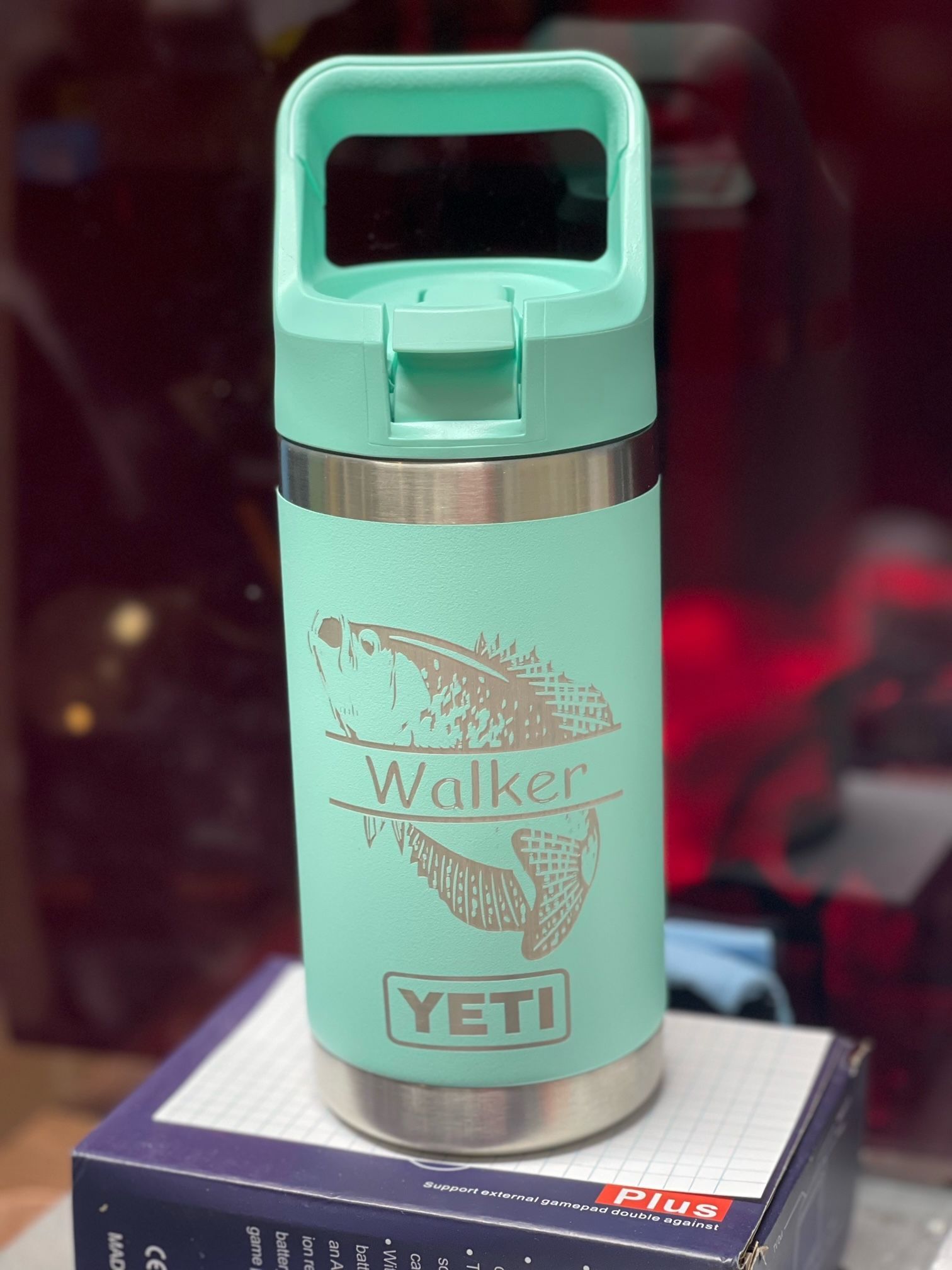 A green yeti bottle with a fish on it is sitting on top of a box.