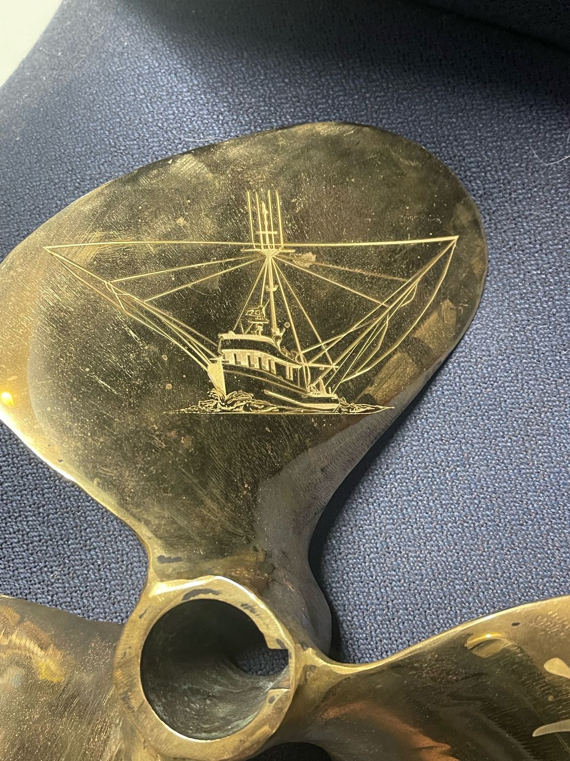 A close up of a brass propeller with a boat on it.