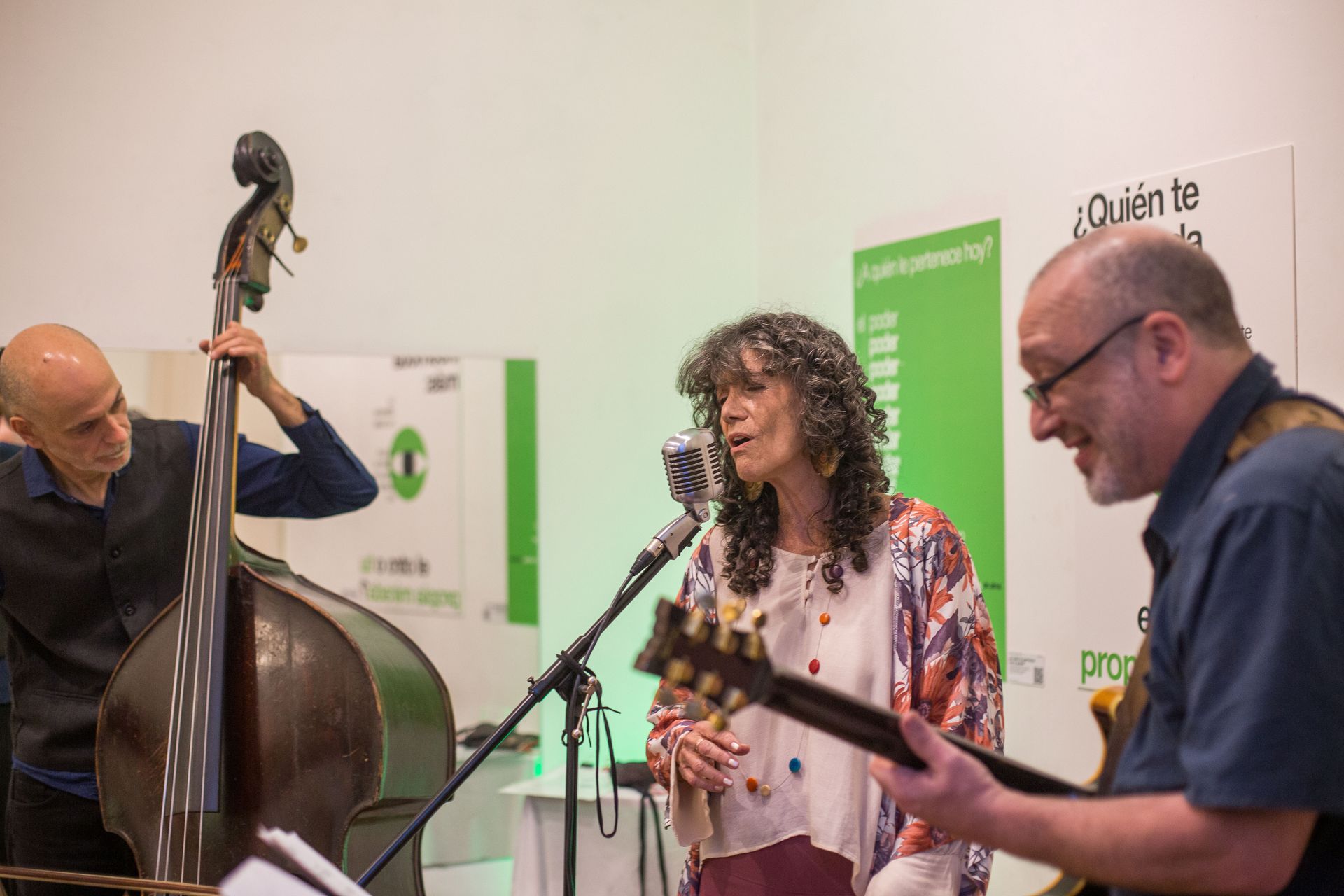 Trío de jazz actuando en interior: cantante, guitarrista y contrabajista.