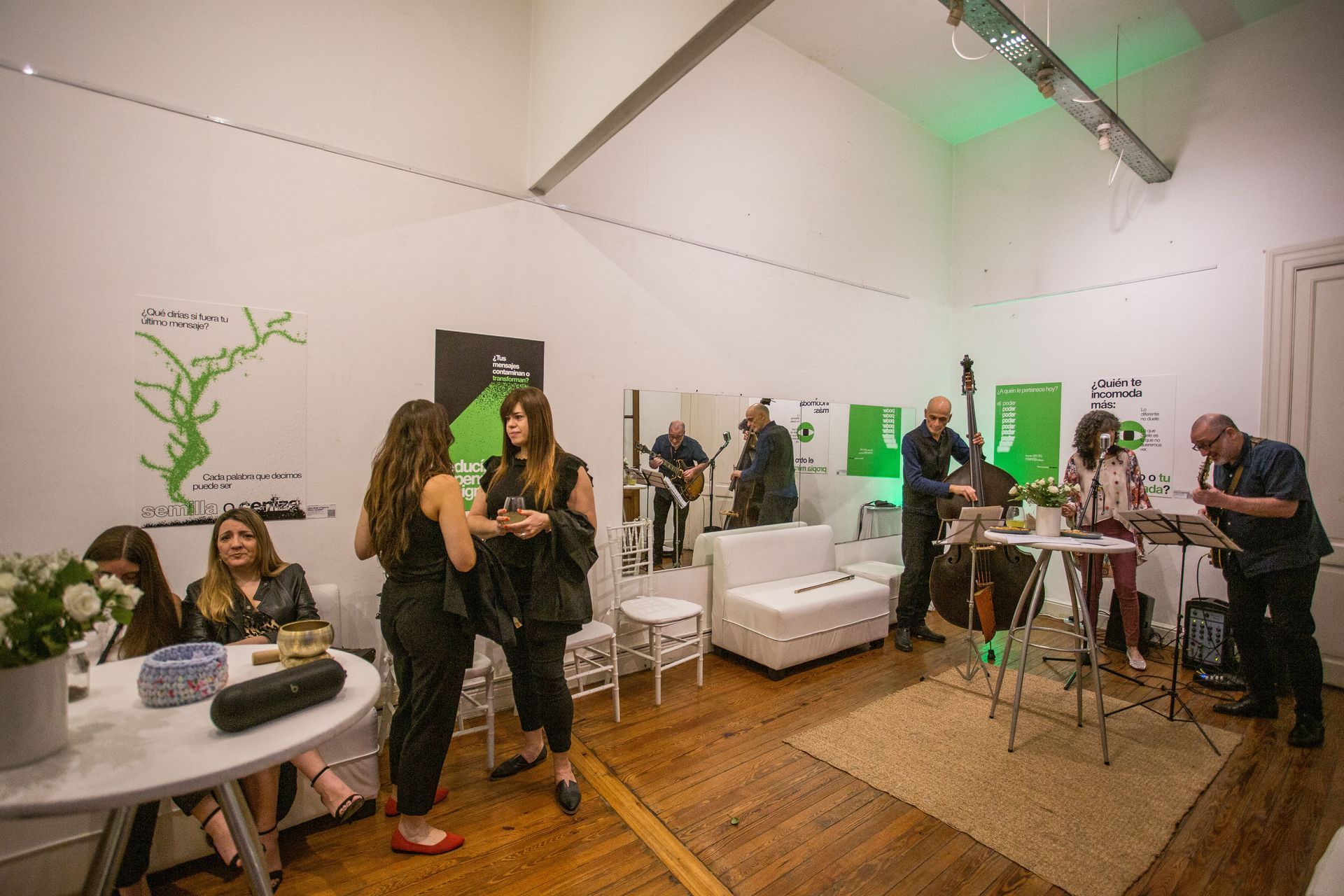 Personas en un evento con una banda tocando música jazz, interior blanco, detalles verdes y pisos de madera.