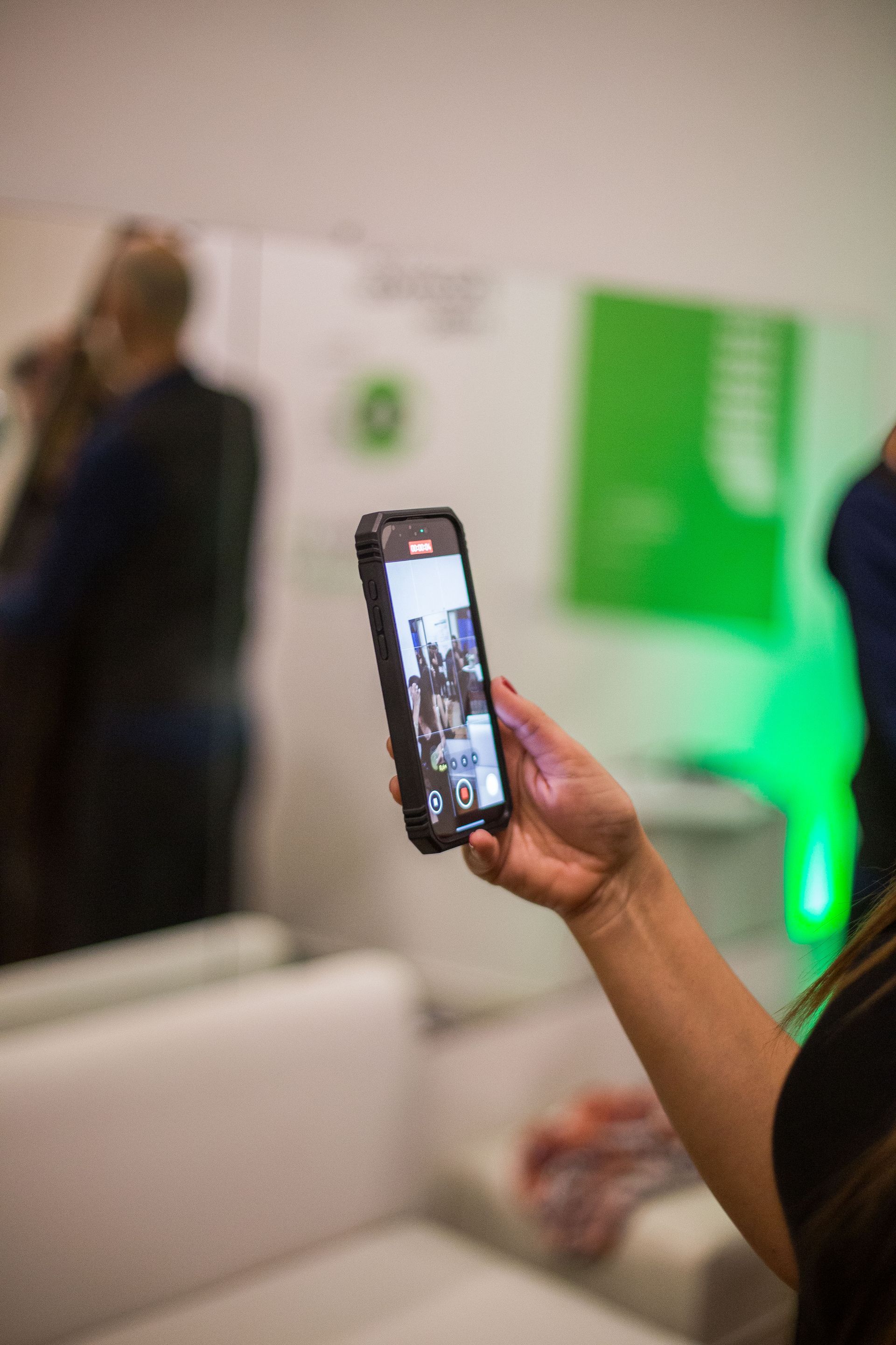 Persona con un teléfono inteligente grabando un video. Interior con detalles en verde y blanco.