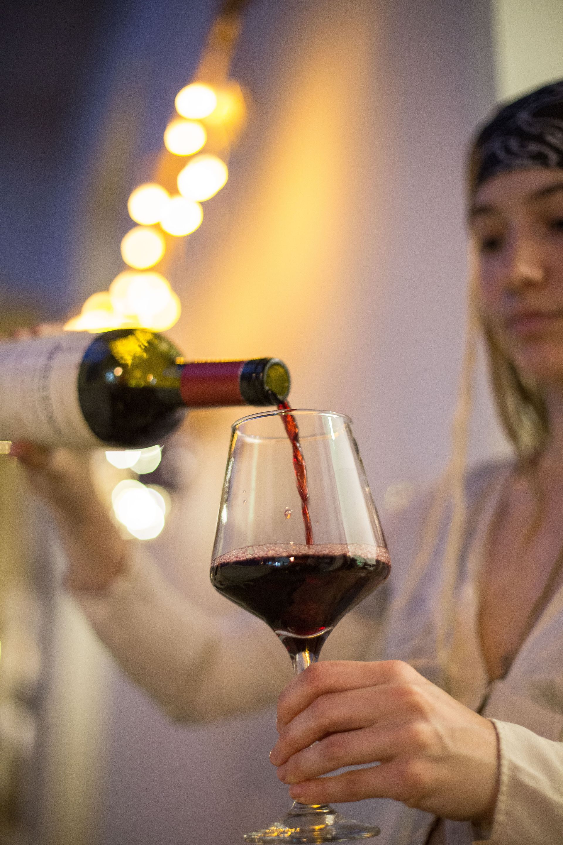 Mujer sirviendo vino tinto en una copa, iluminación cálida de fondo.