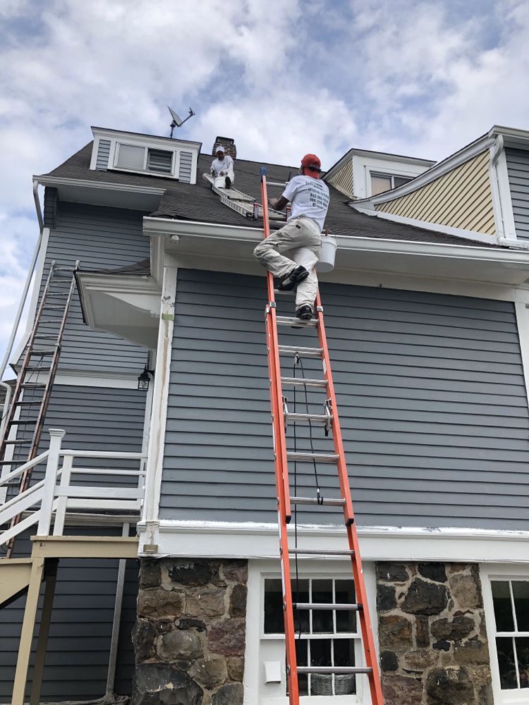 A man is climbing a ladder to paint the roof of a house.