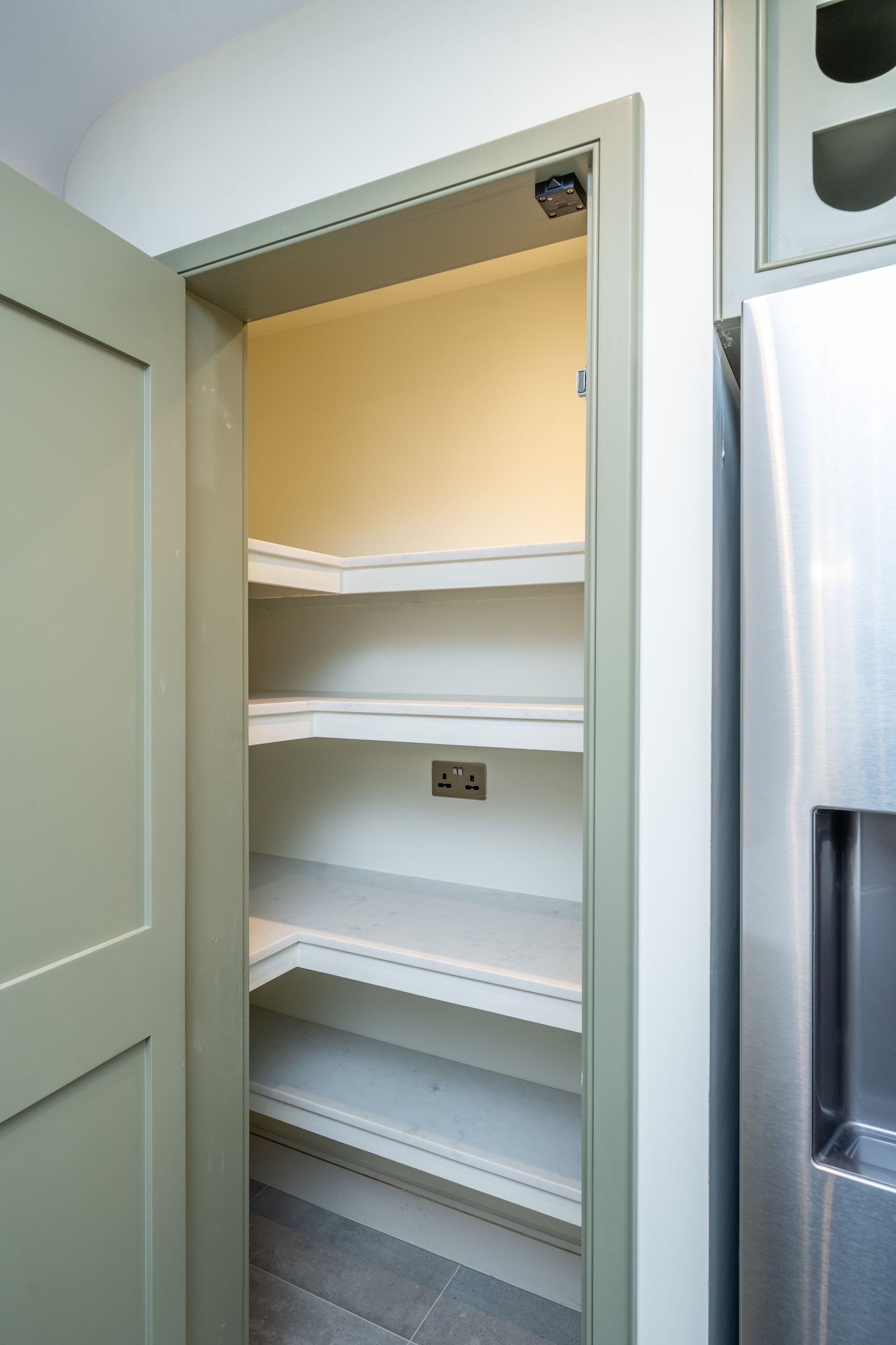 A pantry with shelves next to a refrigerator in a kitchen.
