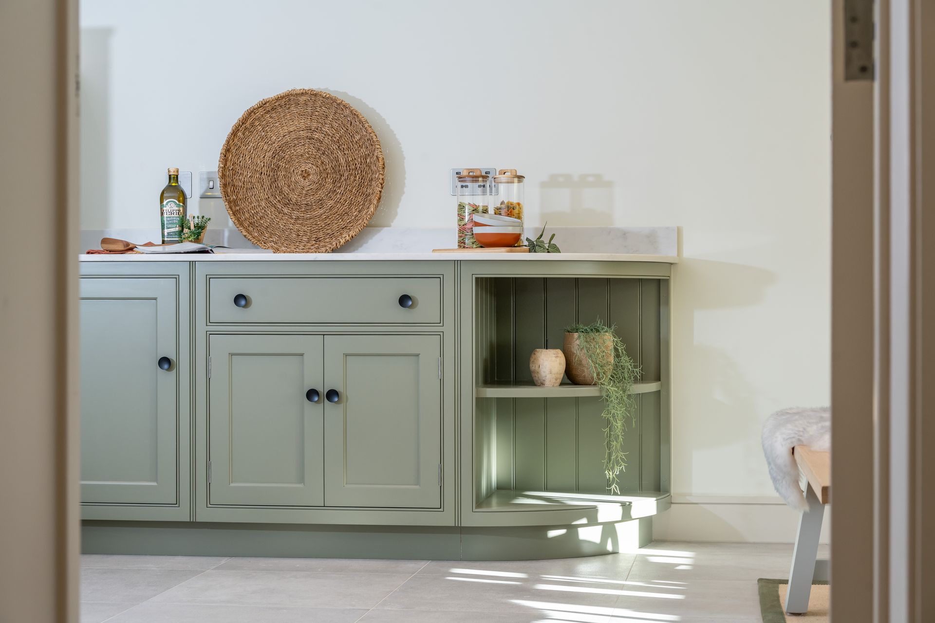 A kitchen with green cabinets and a wicker plate on the counter.