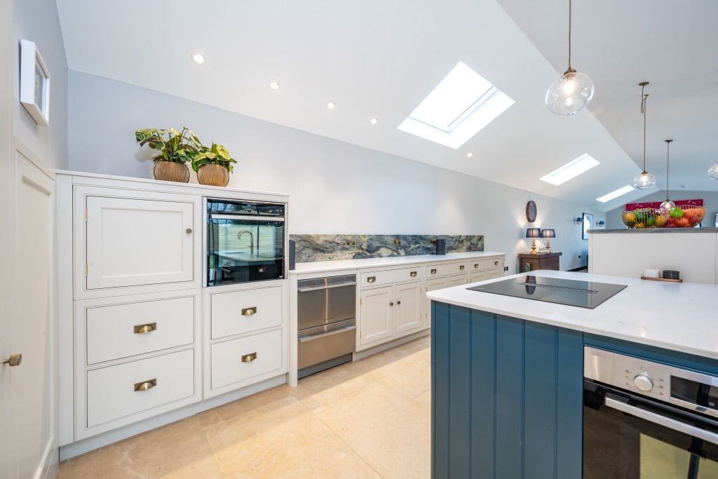 A kitchen with a blue island , white cabinets , stainless steel appliances and a skylight.
