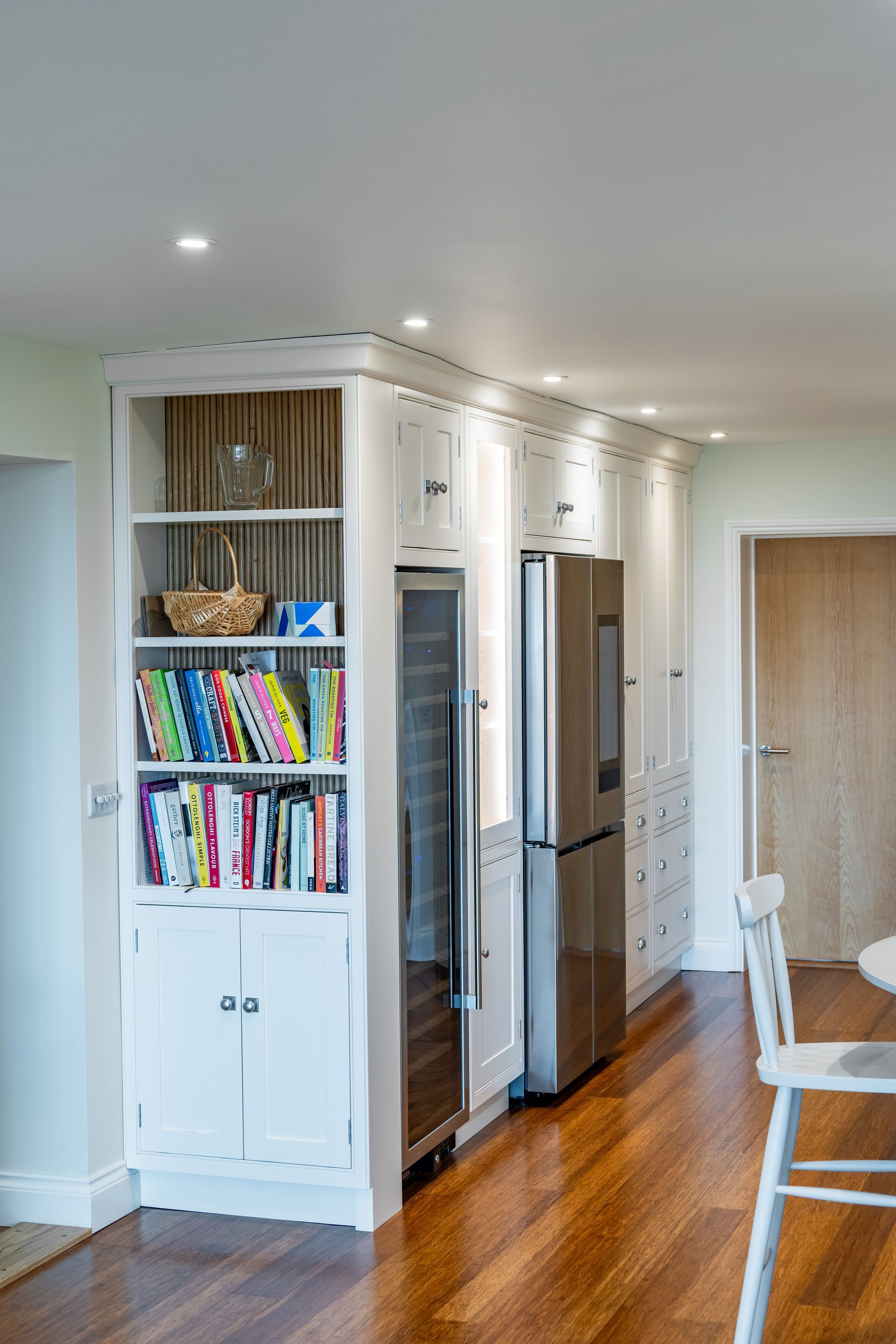 A kitchen with a stainless steel refrigerator and a bookshelf filled with books.