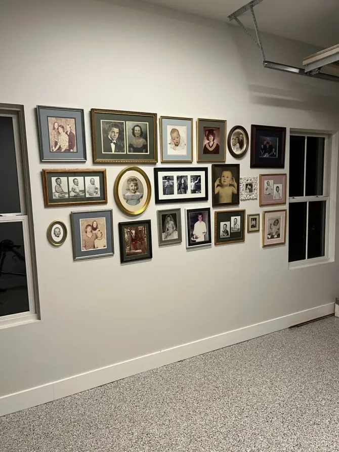 A gallery wall displaying many framed photos and portraits of various sizes on a plain wall between two windows.