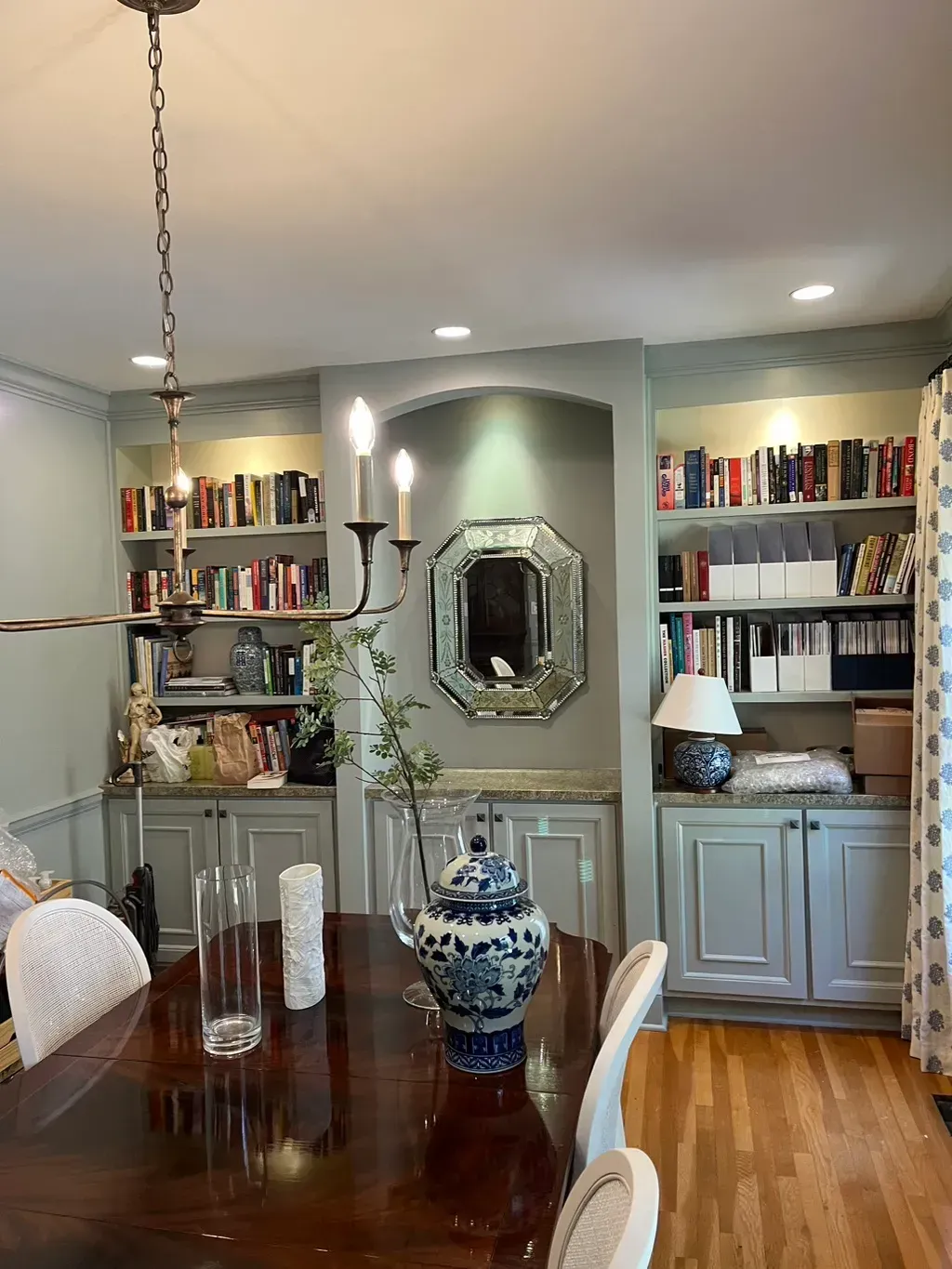 A formal dining room featuring a dark wood table, chandelier, and gray built-in bookshelves flanking a decorative mirror.