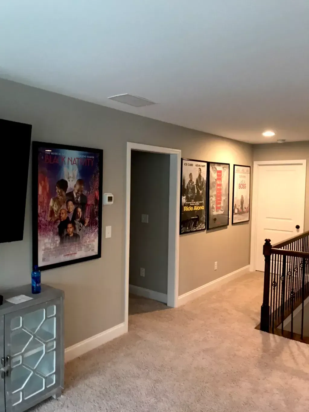 A wall featuring four framed movie posters leading to an open doorway and a staircase in a carpeted home interior.
