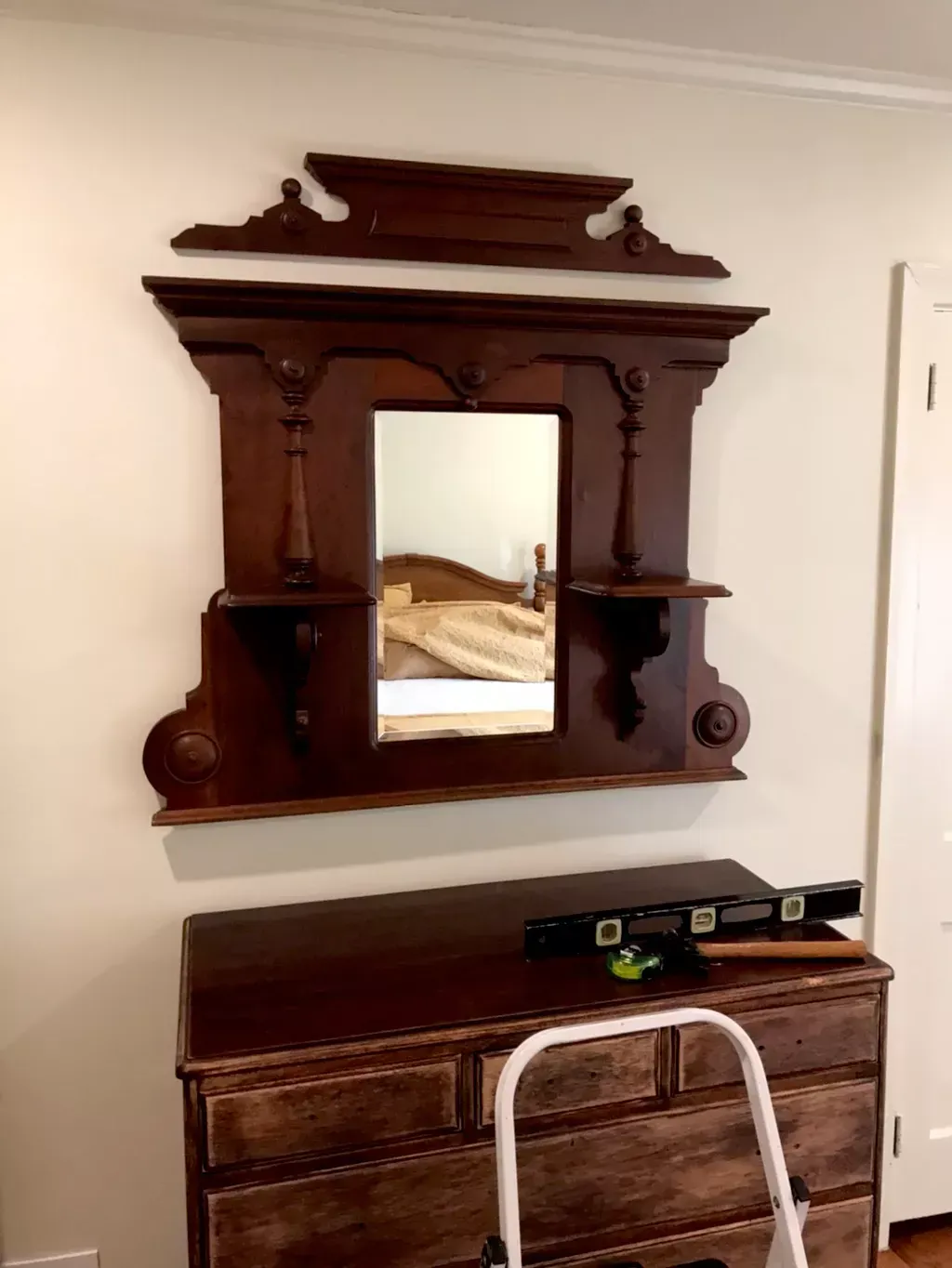 A dark wood Victorian-style mirror frame hanging above a wooden dresser, with a loose decorative crest piece above it.