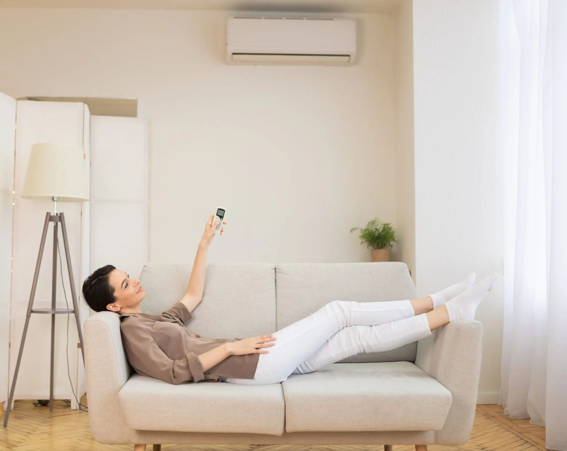Woman lying on couch, using remote to adjust air conditioner in a bright living room. — Careda Air in Saint Georges Basin, NSW 