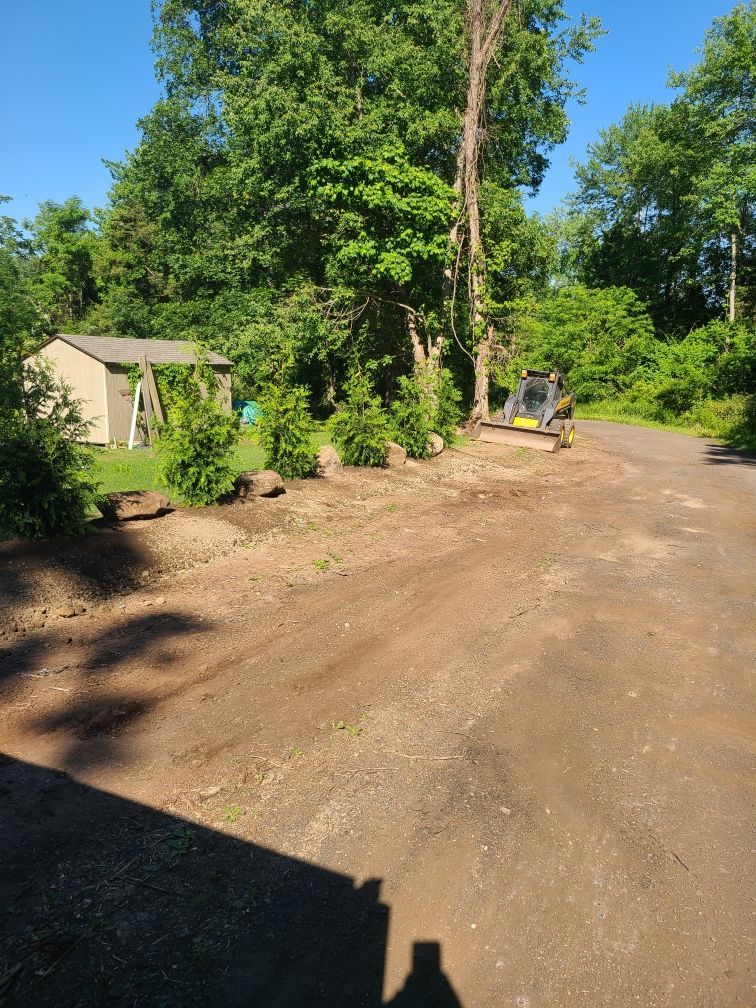 A tractor is driving down a dirt road next to a house.