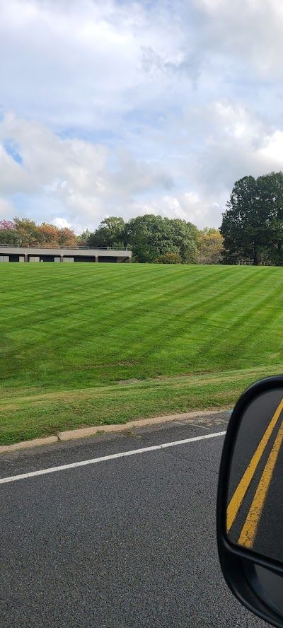 A car is driving down a road next to a grassy field.