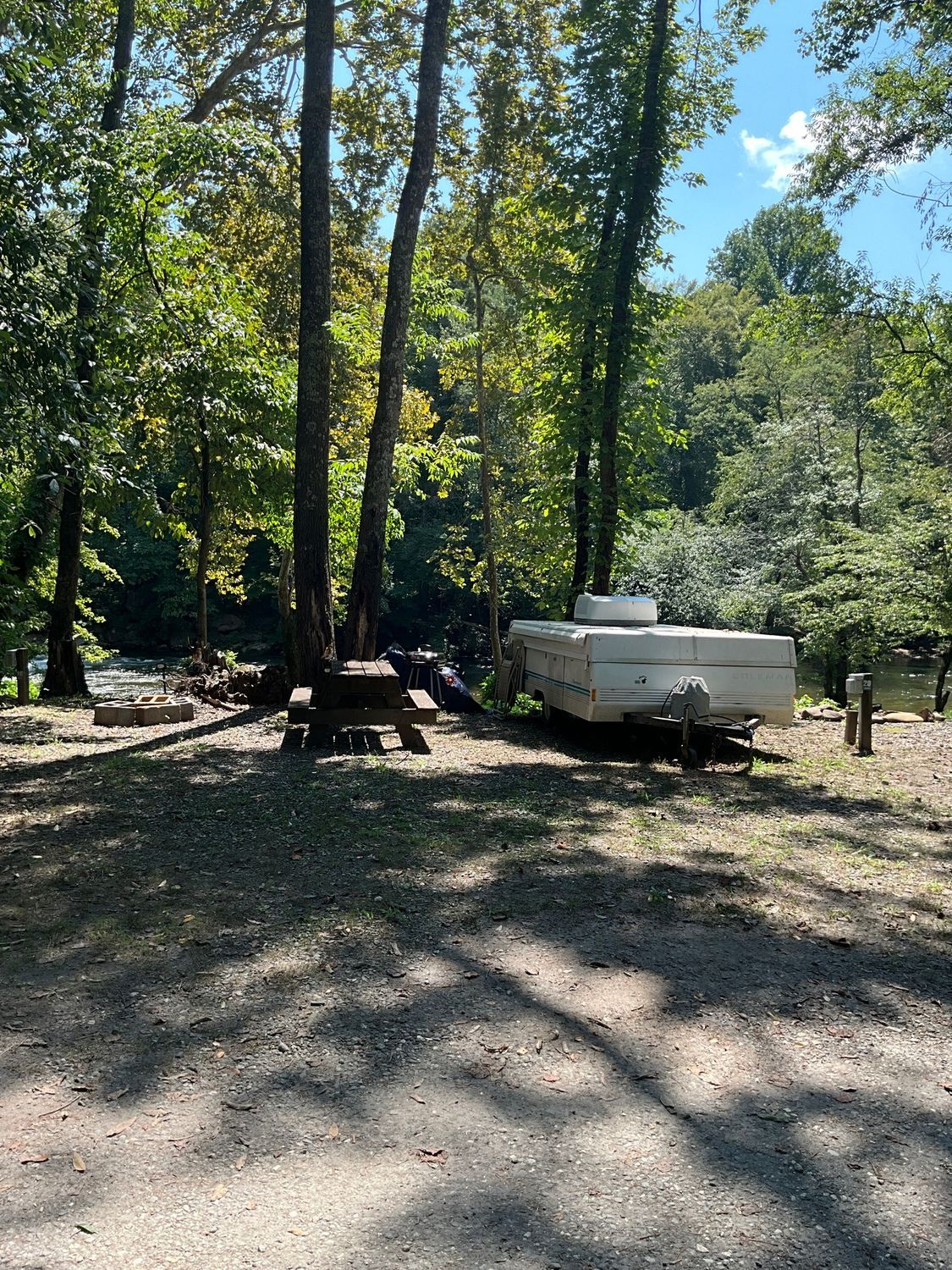 Campsite with a pop-up camper, picnic table, and trees next to a river.