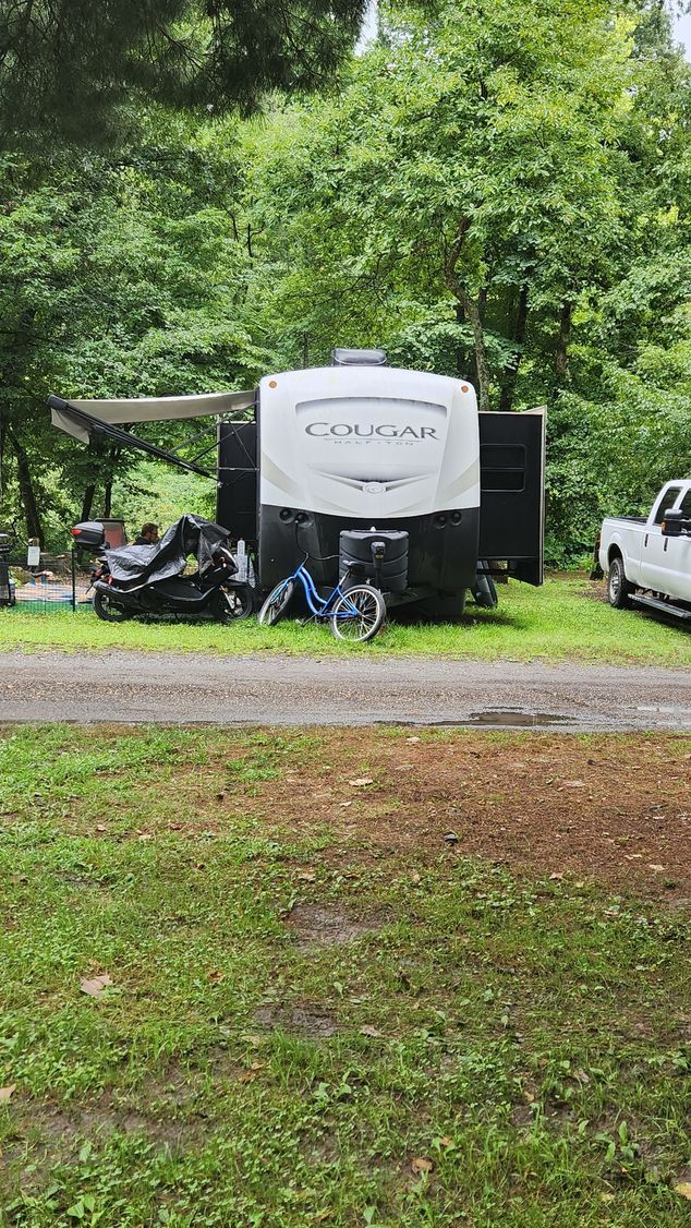 A parked Cougar camper trailer in a grassy area, with trees in the background, and a white truck.