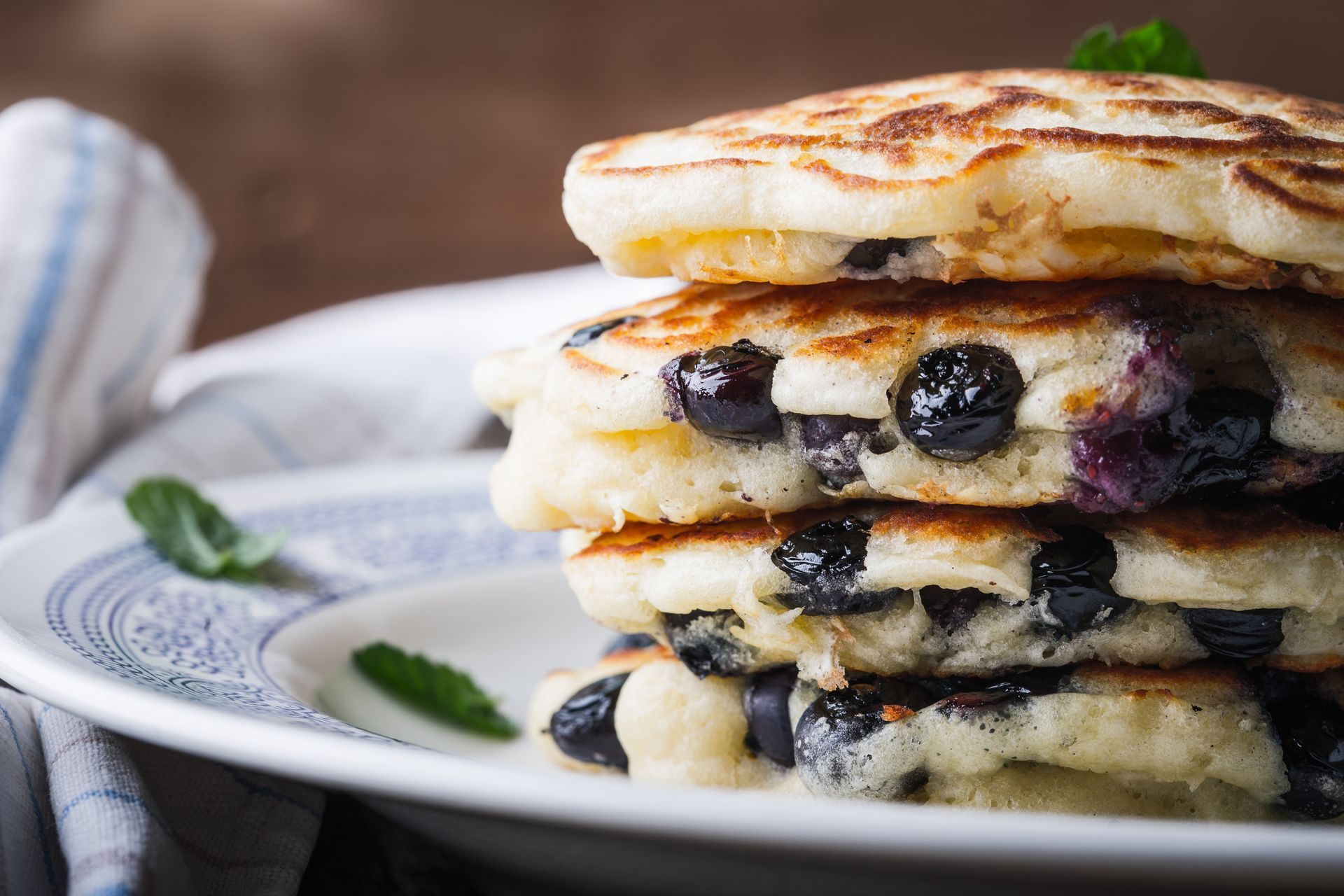 Stack of blueberry pancakes on a white plate, garnished with mint.