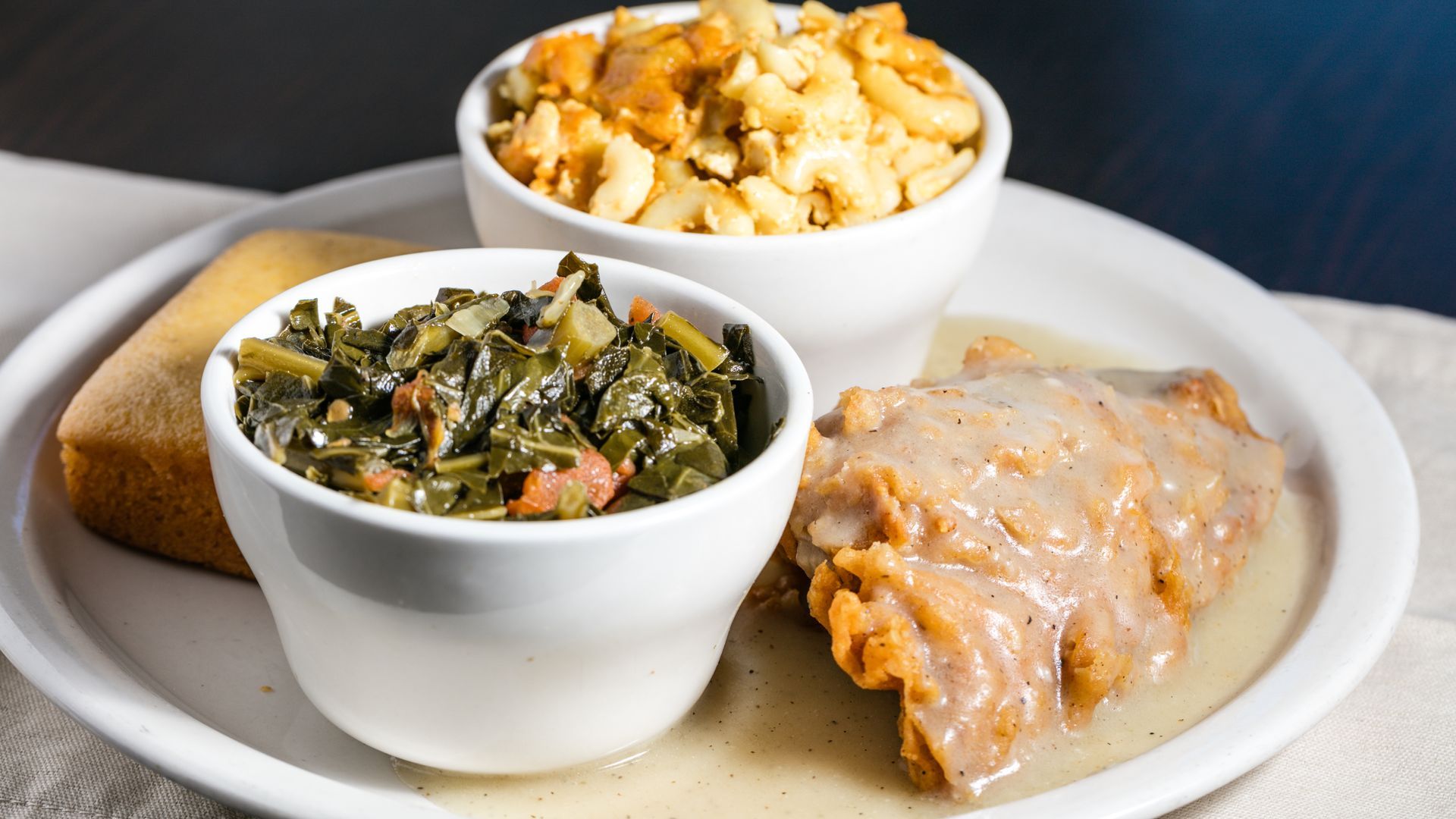 A plate with soul food: mac and cheese, collard greens, fried pork chop with gravy, and cornbread.