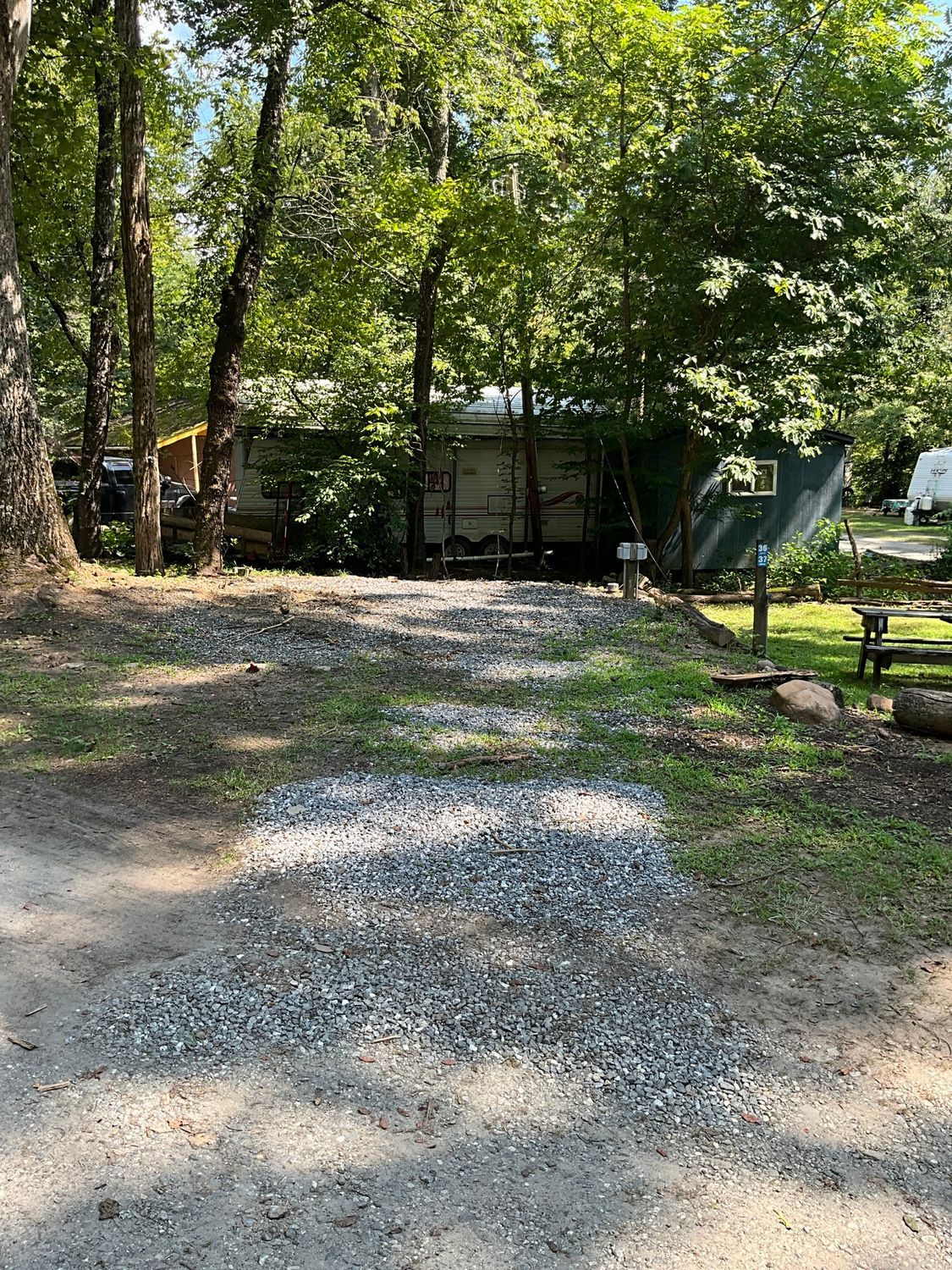 Gravel campsite with RV surrounded by trees. A small shed is on the right.