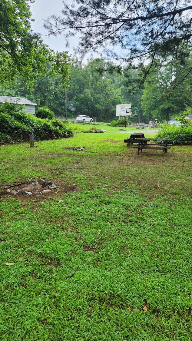 Green grassy yard with picnic table, trees, and a building in the background.