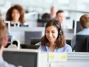 A woman wearing a headset is sitting at a desk in a call center.