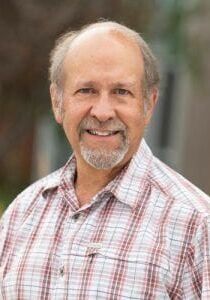 A man with a beard is wearing a plaid shirt and smiling for the camera.