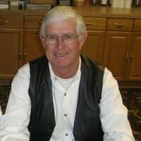 A man wearing glasses and a leather vest is sitting at a table.