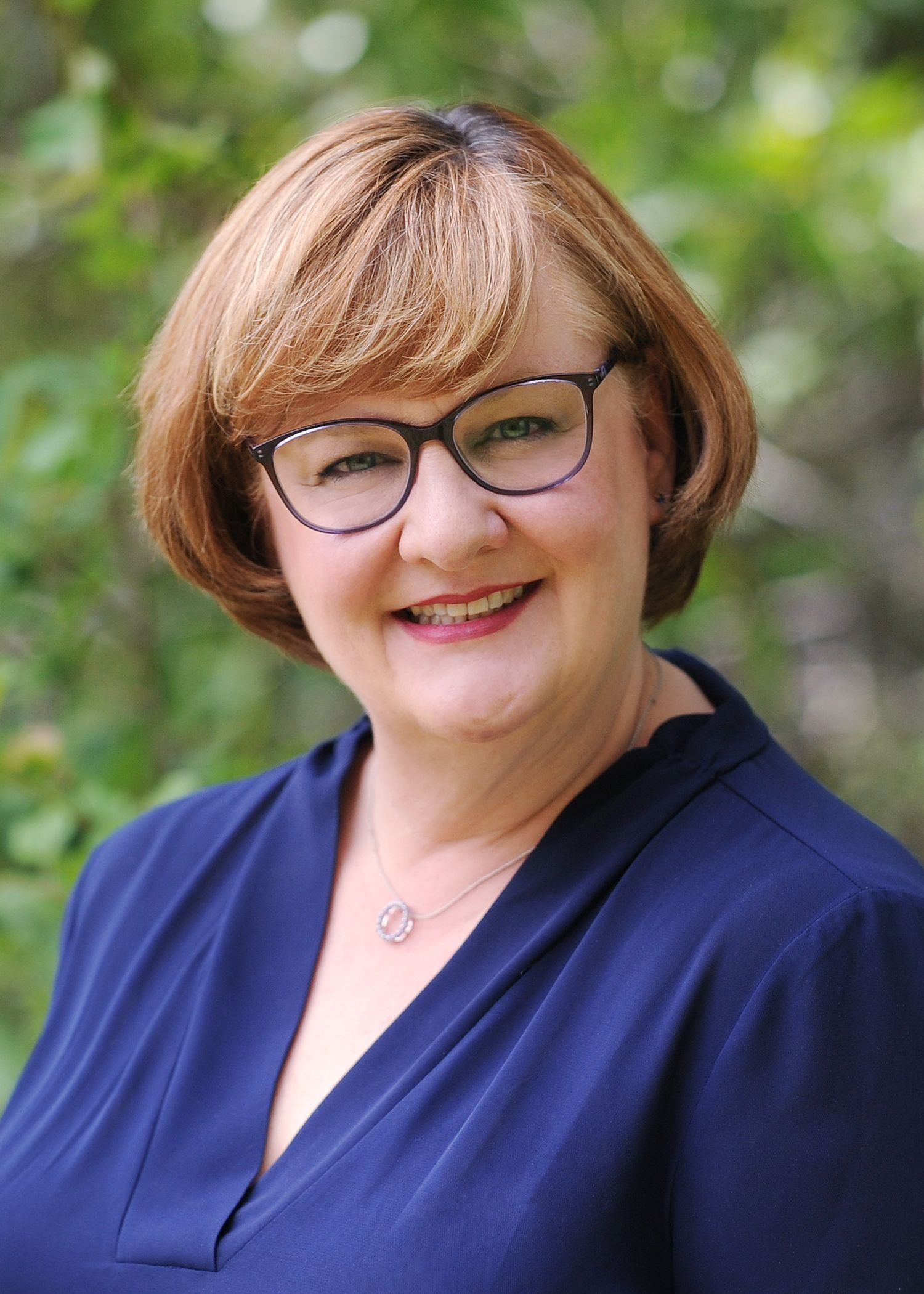 A bald man wearing glasses and a blue shirt is smiling for the camera.