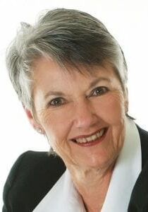 A woman in a suit and white collared shirt is smiling for the camera.