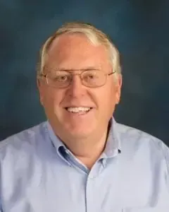 A man wearing glasses and a blue shirt is smiling for the camera.