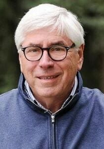 A man wearing glasses and a blue jacket is smiling for the camera.