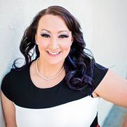 A woman with long brown hair is smiling and wearing a black shirt.